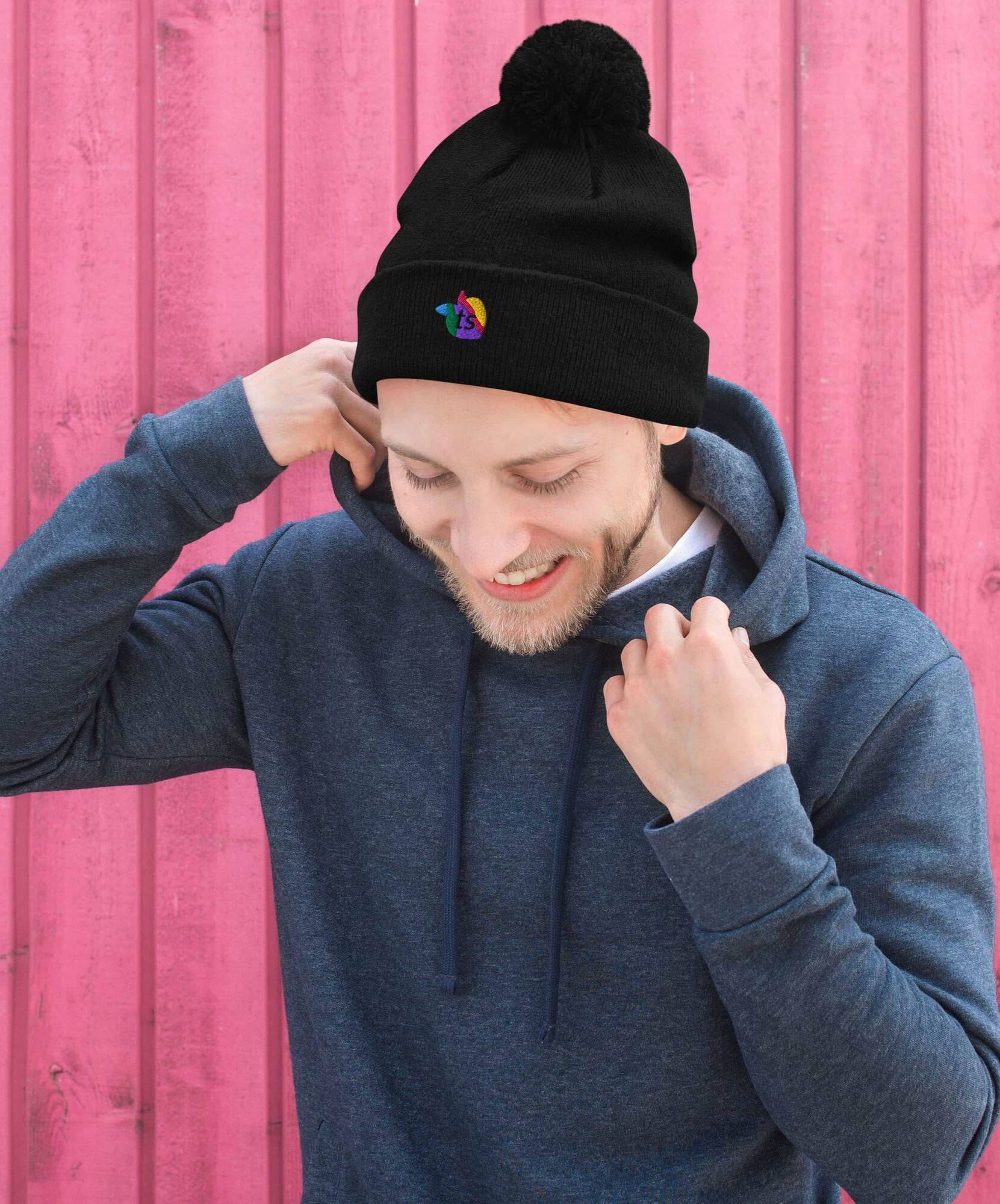Man wearing a black beanie with a colorful logo against a pink wooden background